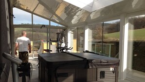 A modern outdoor hot tub area with a glass enclosure, wooden deck, and exercise equipment. - Les Chambres d'Hôtes du Mont Monnet (Longes)