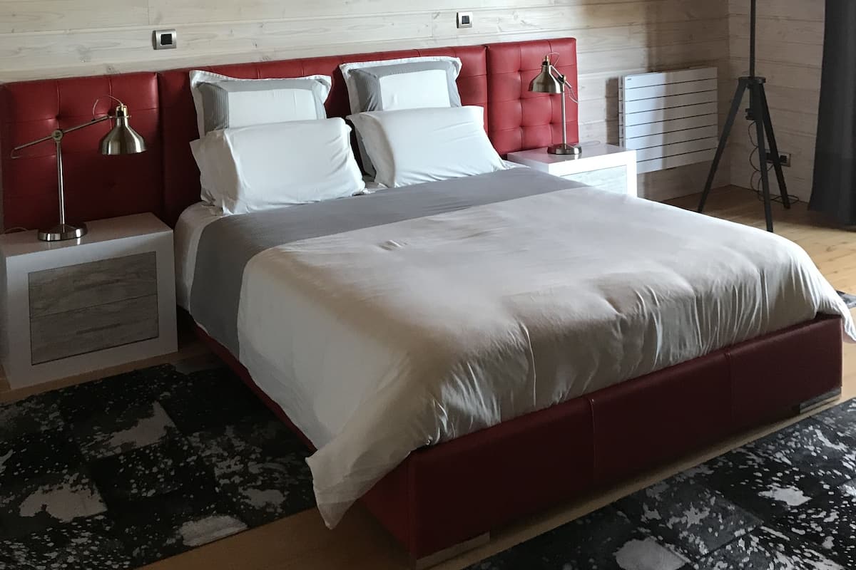 Ein modernes Schlafzimmer mit einem roten Kopfteil, einem großen abstrakten Gemälde, einer schwarzen Stehlampe und einer weißen Bettdecke.