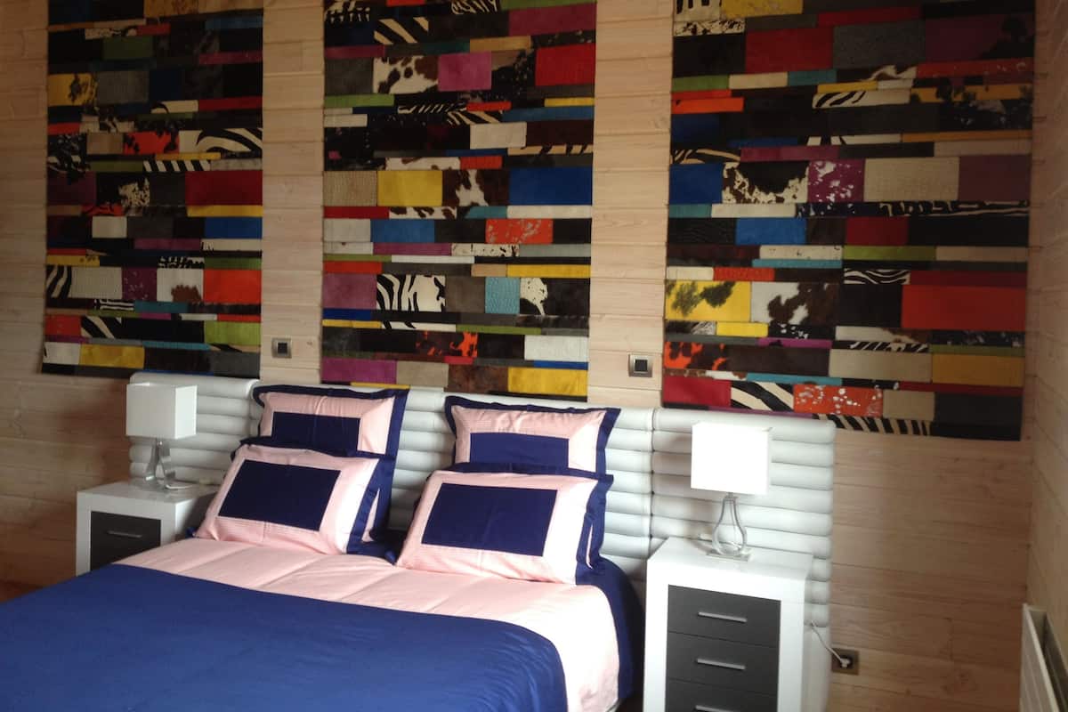 Ein Schlafzimmer mit einem Bett, zwei Nachttischen, einem Beistelltisch und einem farbenfrohen abstrakten Kunstwerk über dem Bett.