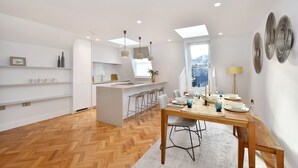 A modern kitchen with a central island, bar stools, and a dining area with a wooden table and chairs. - Amazing Mayfair 2 Bed £6 million AC Terrace Wi-Fi (London)