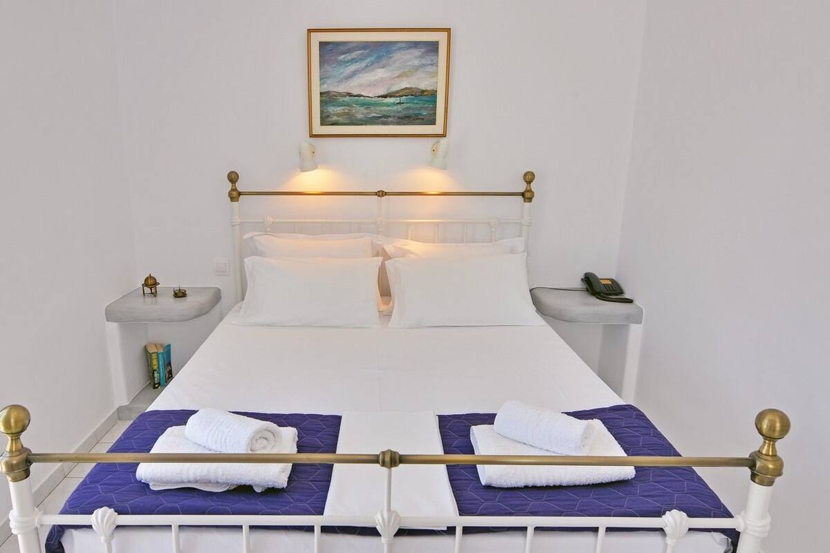A neatly made bed with a white and purple bedspread, two white towels, and a gold-framed headboard.