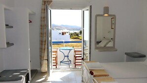 Habitación con vista a un edificio blanco y montañas. Hay una pequeña mesa y dos sillas afuera de la puerta.
