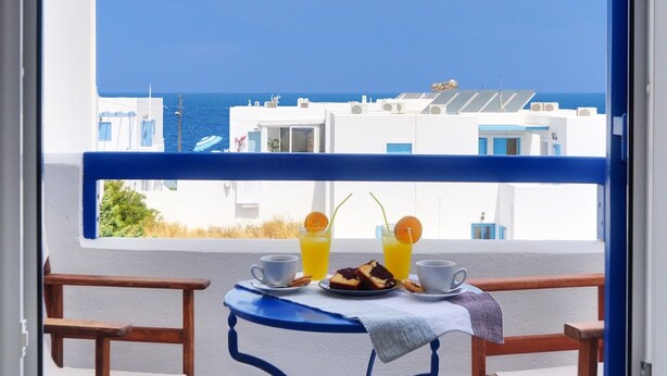 Un balcón con una mesa lista para el desayuno, con vistas a la costa, edificios y el mar.