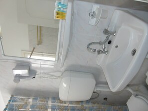A bathroom with a white sink, toilet, and mirror. There is a window above the sink, and a towel rack is visible.