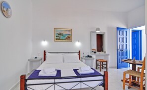 A hotel room with a bed, a bathroom, a small table with a chair, and a blue door.