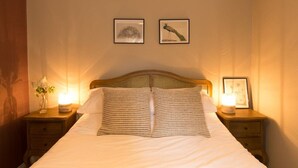Quarto de hotel com uma cama grande, duas mesas de cabeceira com abajures e duas molduras na parede.