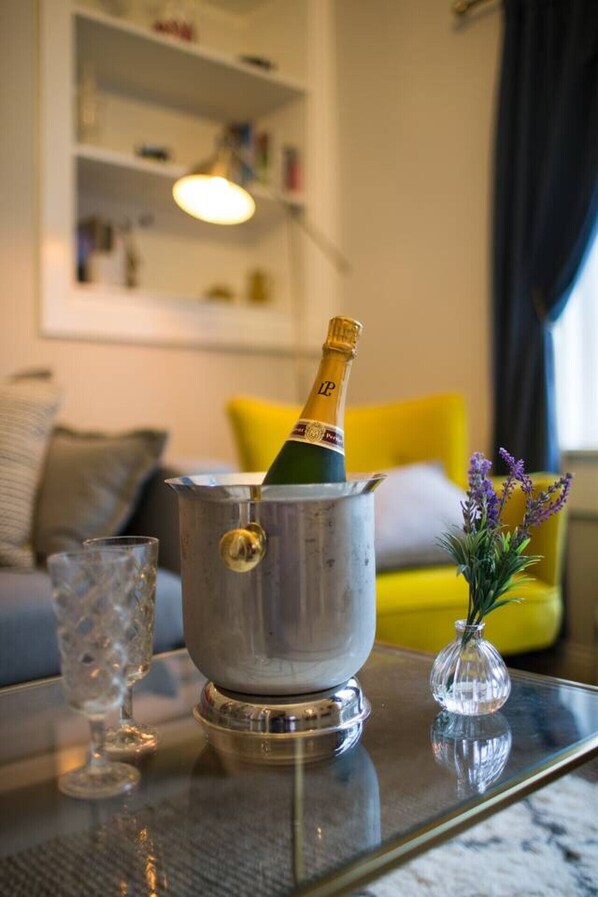 A champagne bottle in a metal bucket on a glass table, with a glass and a vase of flowers nearby.