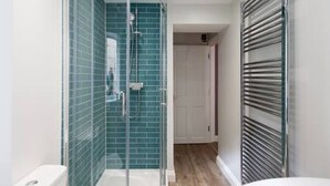 Un bany modern amb un cubicle de dutxa de vidre, un vàter blanc i una barra de tovalloles.