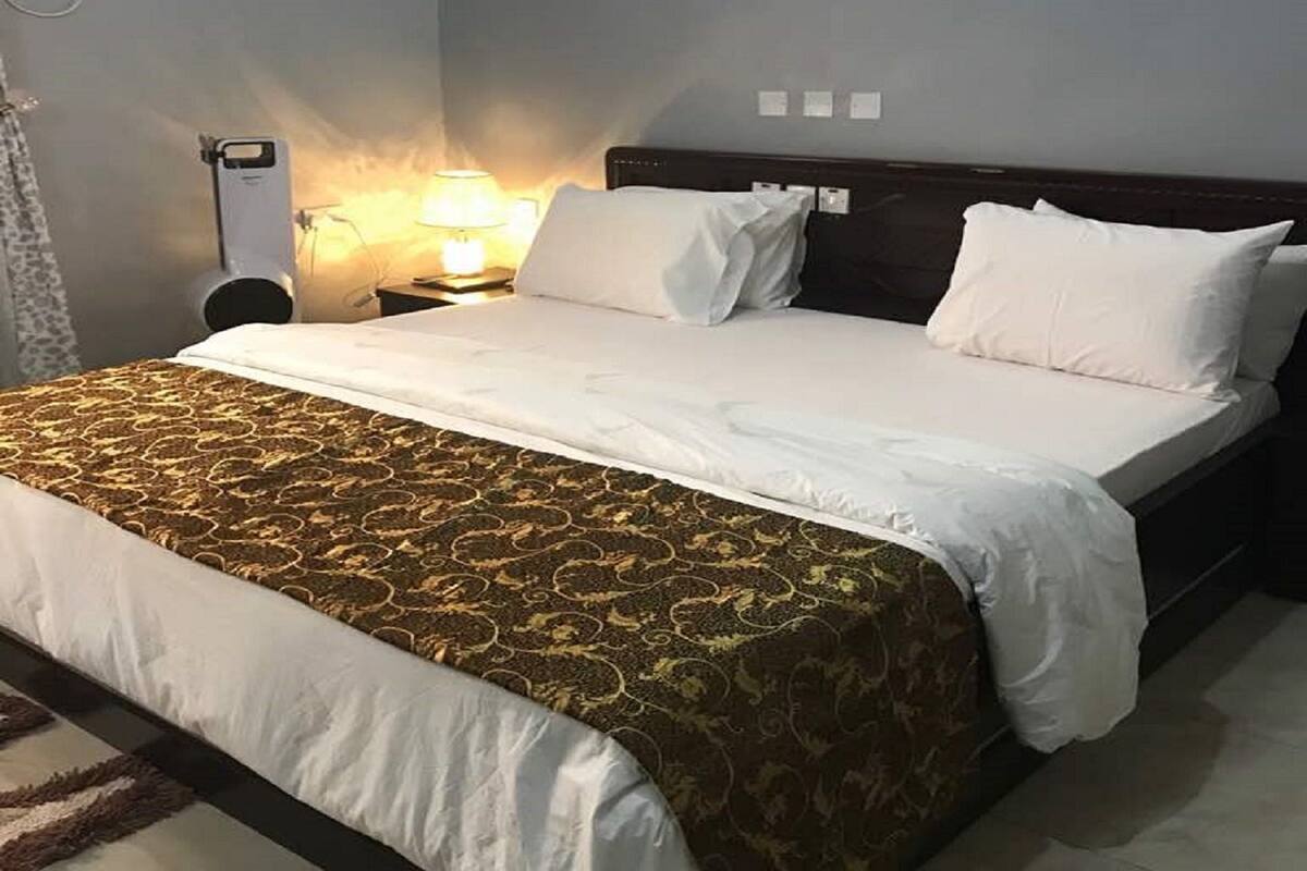 Una habitación de hotel con una cama, una mesita de noche, una lámpara y un equipo de aire acondicionado.