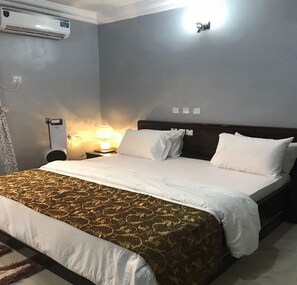 Una habitación de hotel con una cama, una mesita de noche, una lámpara y un equipo de aire acondicionado.
