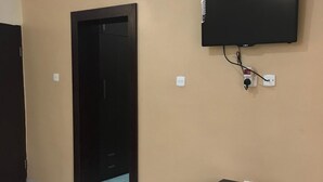 A room with a closed door, a television mounted on the wall, and a small cabinet. - Jim-Eddy Suites (Enugu)