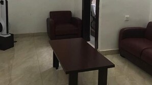 A room with a dark wooden table, a red sofa, and a white air conditioning unit. - Jim-Eddy Suites (Enugu)