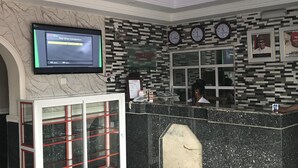 A hotel reception area with a digital screen displaying a welcome message, a reception desk, a chandelier, and a mosaic wall. - Jim-Eddy Suites (Enugu)