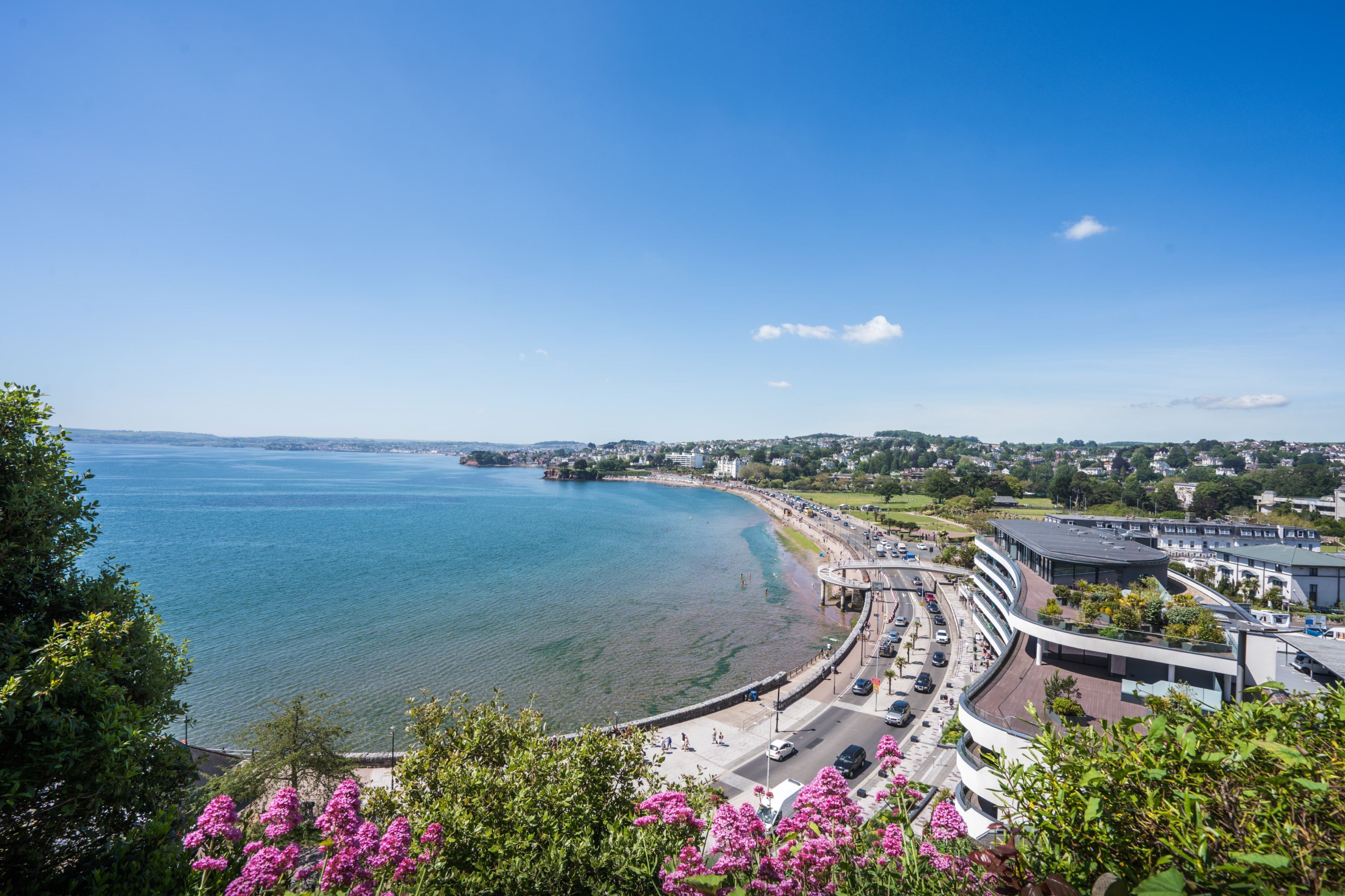 A coastal cityscape with a curved road, a beach, and a modern building complex.