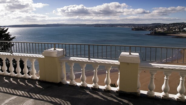 A balcony with a view of the sea and a distant shoreline.