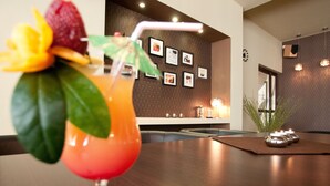 Un coin bar avec un cocktail posé sur la table, des tableaux encadrés au mur et une plante sur le côté.