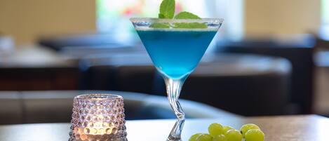 A martini glass with a blue liquid and mint garnish on a table with a textured placemat.