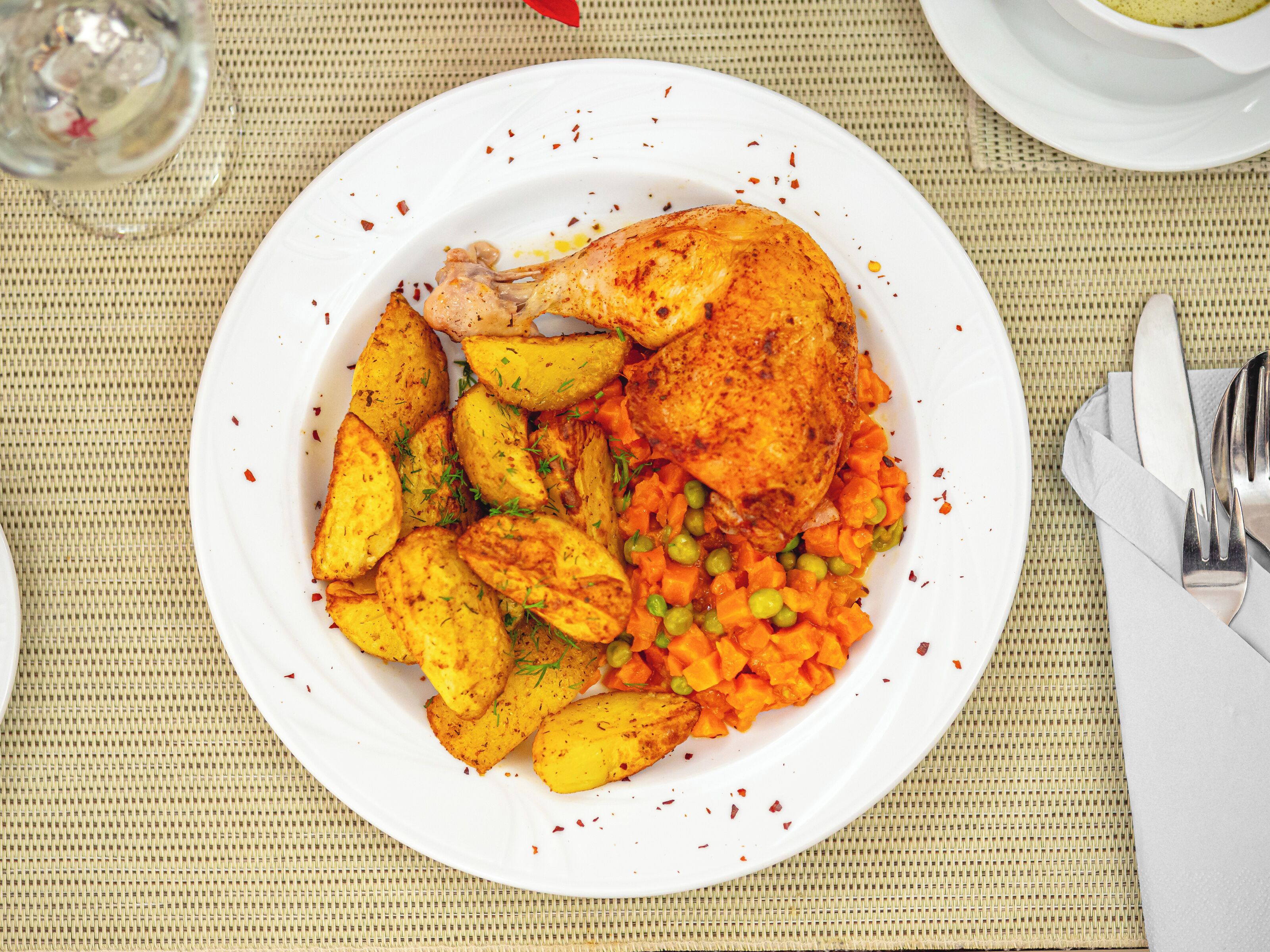 A plate with a roasted chicken, potatoes, and carrots.