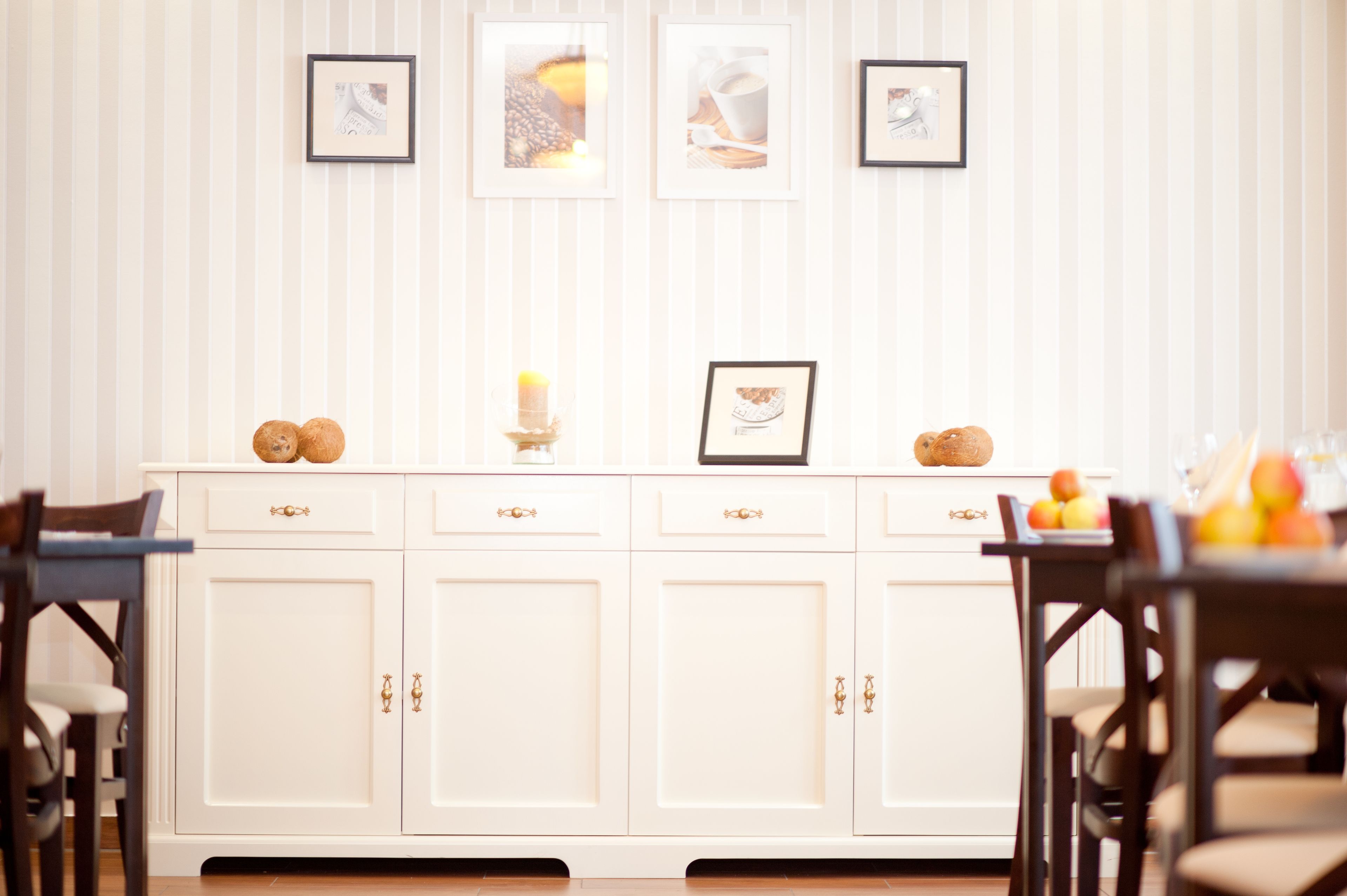 A white kitchen with four cabinets, a central island with a candle, and framed pictures on the wall.