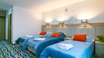Ein Hotelzimmer mit zwei Betten, jeweils mit blauer Bettwäsche und orangefarbenen Kissen, einer Wandmalerei und einem gemusterten Teppich.