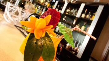 A cocktail with a strawberry and flower garnish on a bar counter.