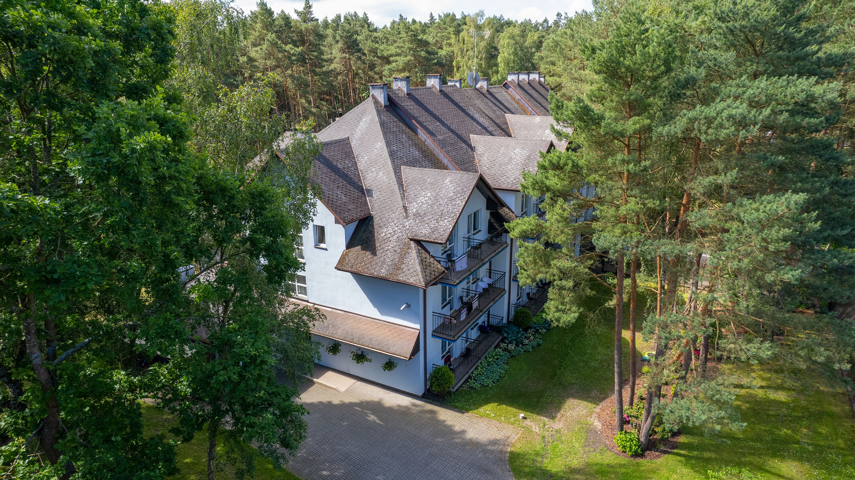 A multi-story building with a sloped roof, surrounded by dense trees.