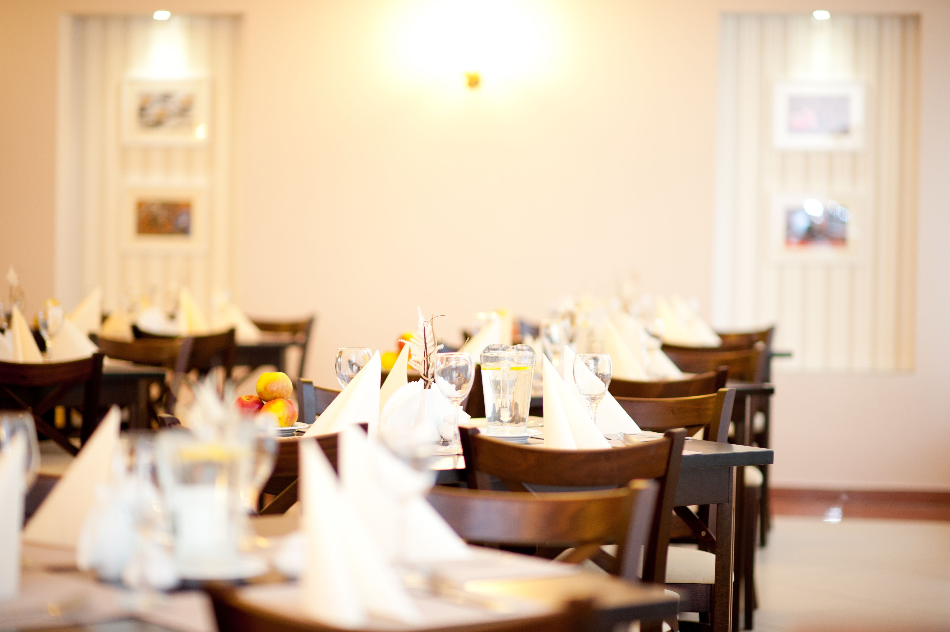 A dining area with tables set for service, featuring neatly arranged napkins, glasses, and a fruit bowl.