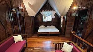 A cozy attic bedroom with a wooden sloped ceiling, a bed, two red sofas, and a large window. - Waterfront villa with live-in staff! (NOSY BE)