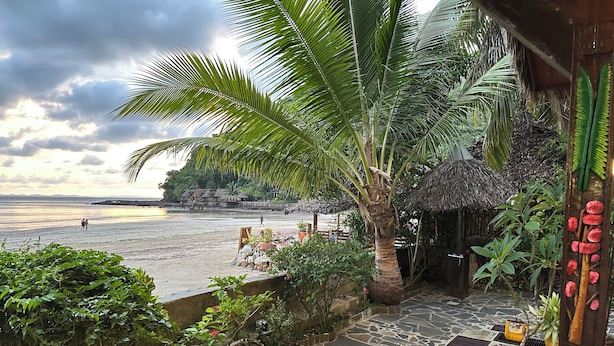 A tropical beach scene with a stone pathway leading to a thatched-roof structure. - Waterfront villa with live-in staff! (NOSY BE)