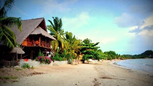 A beachside resort with thatched-roof structures, palm trees, and a sandy beach. - Waterfront villa with live-in staff! (NOSY BE)