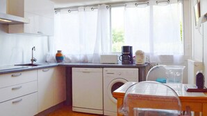 A compact kitchen with a washing machine, a coffee maker, and a window with curtains.
