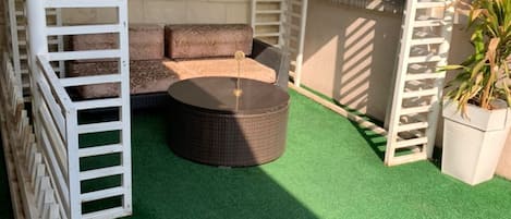 A covered outdoor seating area with a round table and cushioned seating.