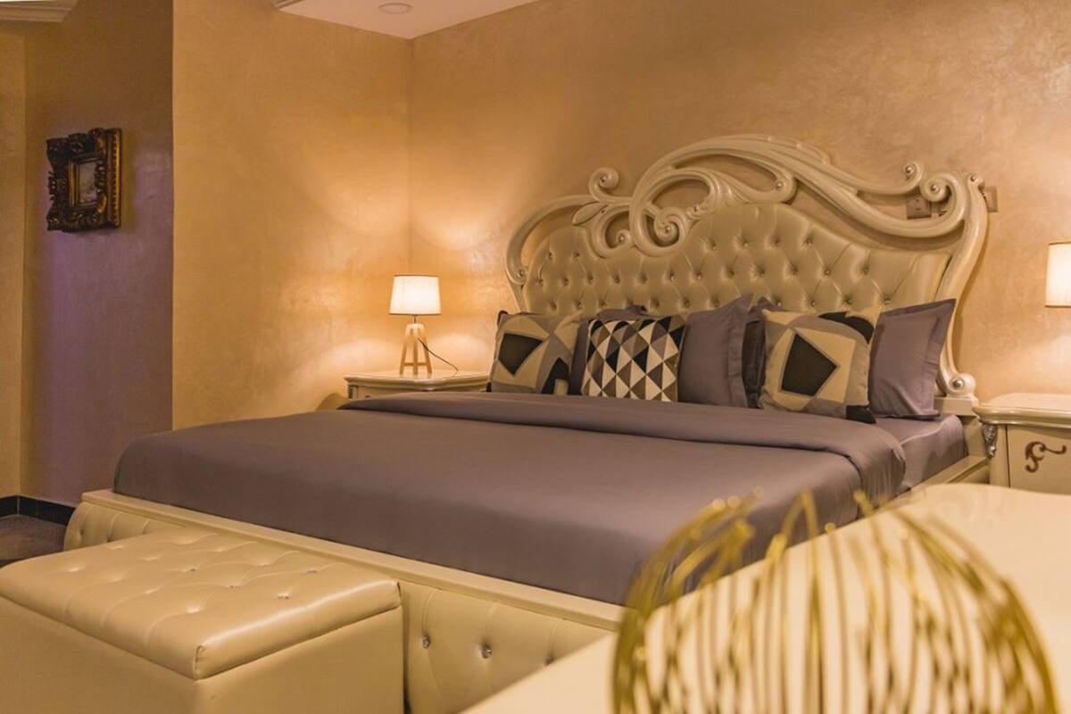 Une chambre à coucher bien aménagée, avec un grand lit, une table de chevet dotée d’une lampe et un élément décoratif mural.