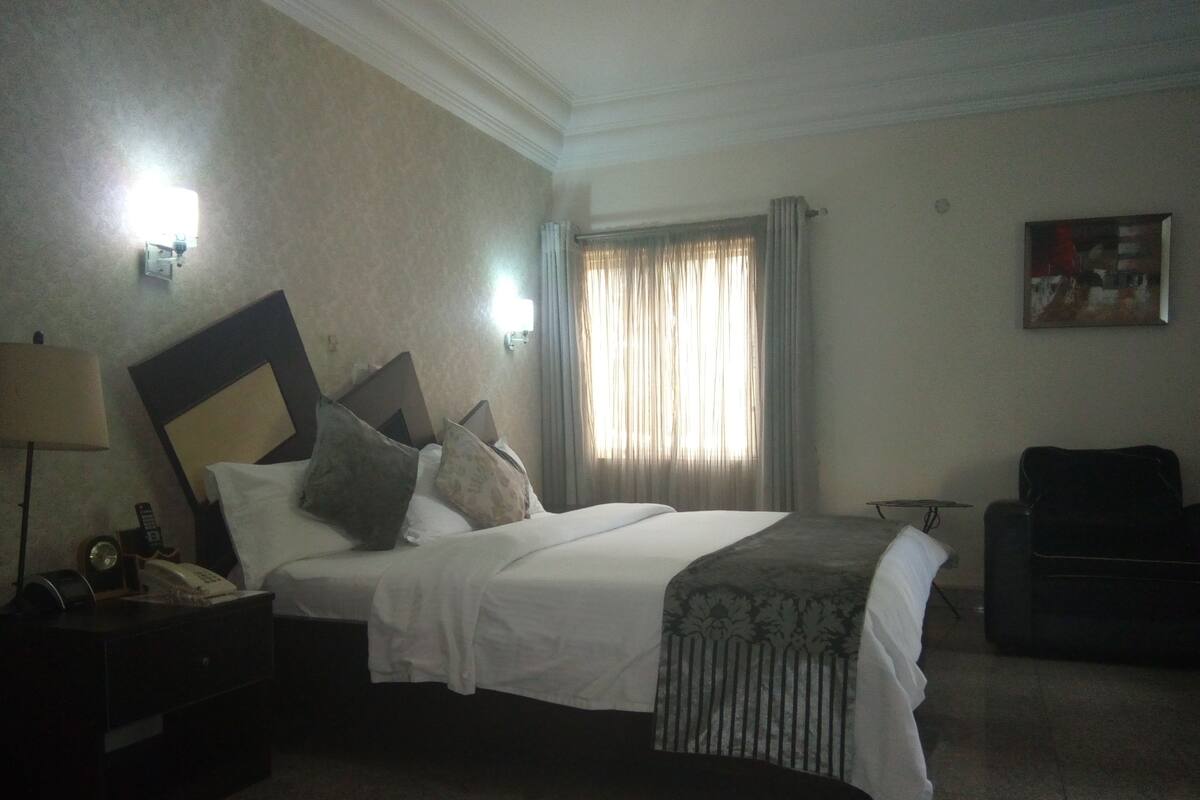 Une chambre d’hôtel avec un grand lit, une table de chevet avec une lampe, une chaise et un tableau au mur.