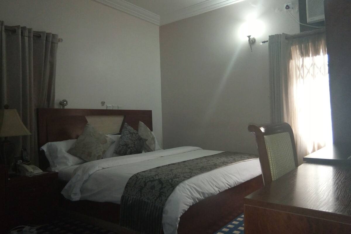 Une chambre d’hôtel équipée d’un lit, d’un bureau, d’une chaise, d’une lampe et d’un appareil de climatisation.