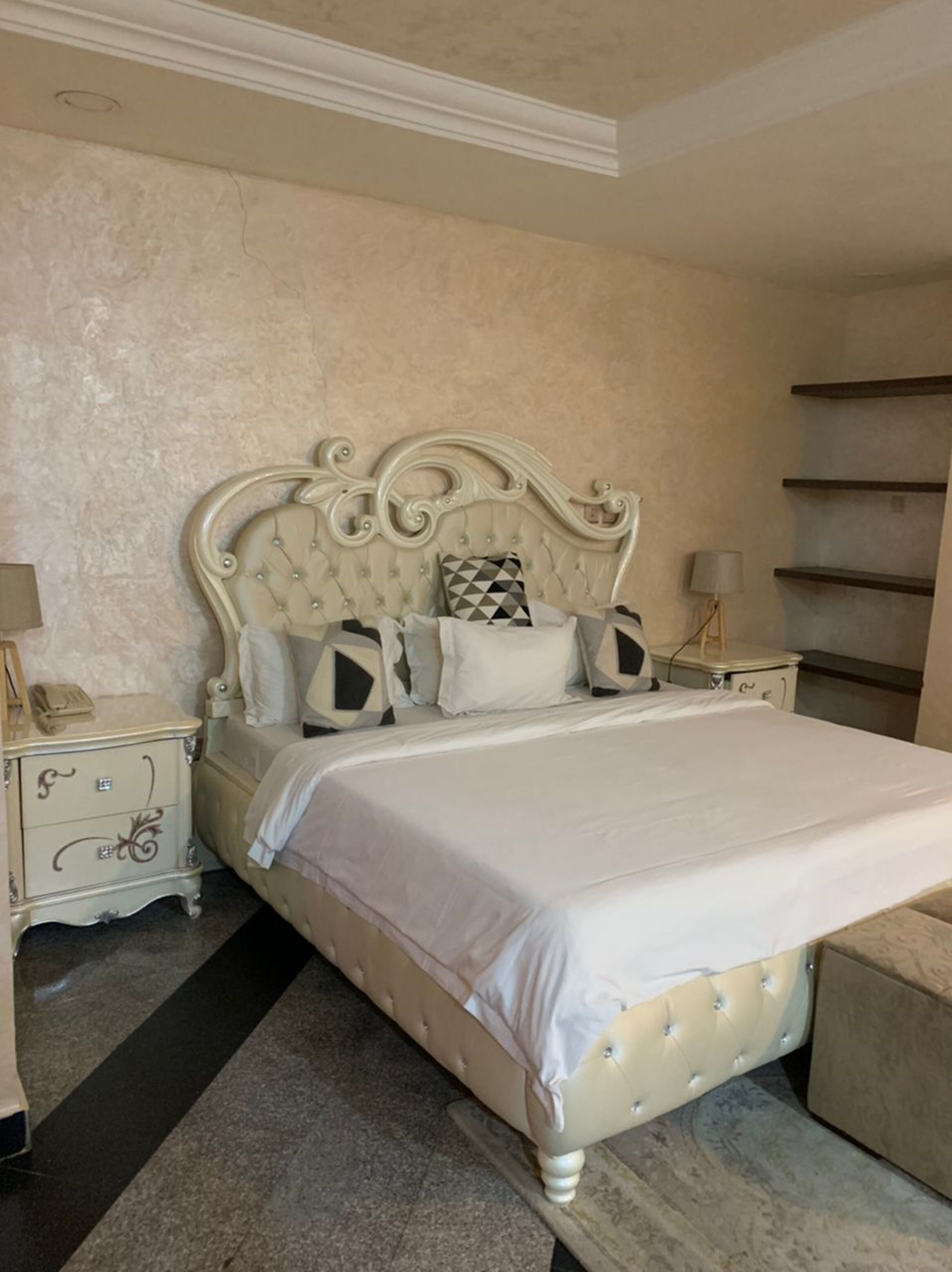 A bedroom with a large bed, a nightstand, a lamp, and a shelf unit.