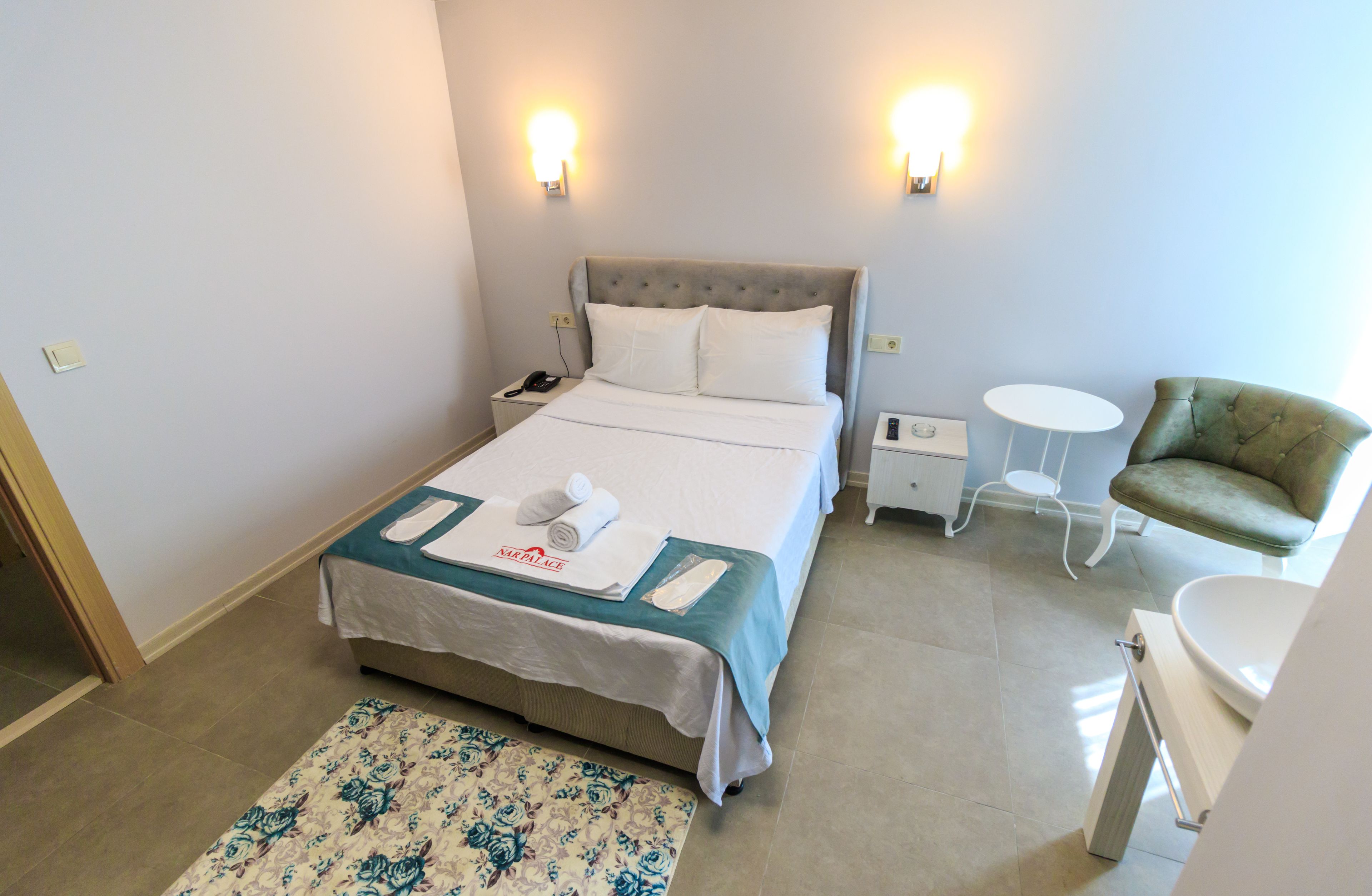Habitació d'hotel amb llit, taules de nit, una cadira, taula petita rodona i bany.