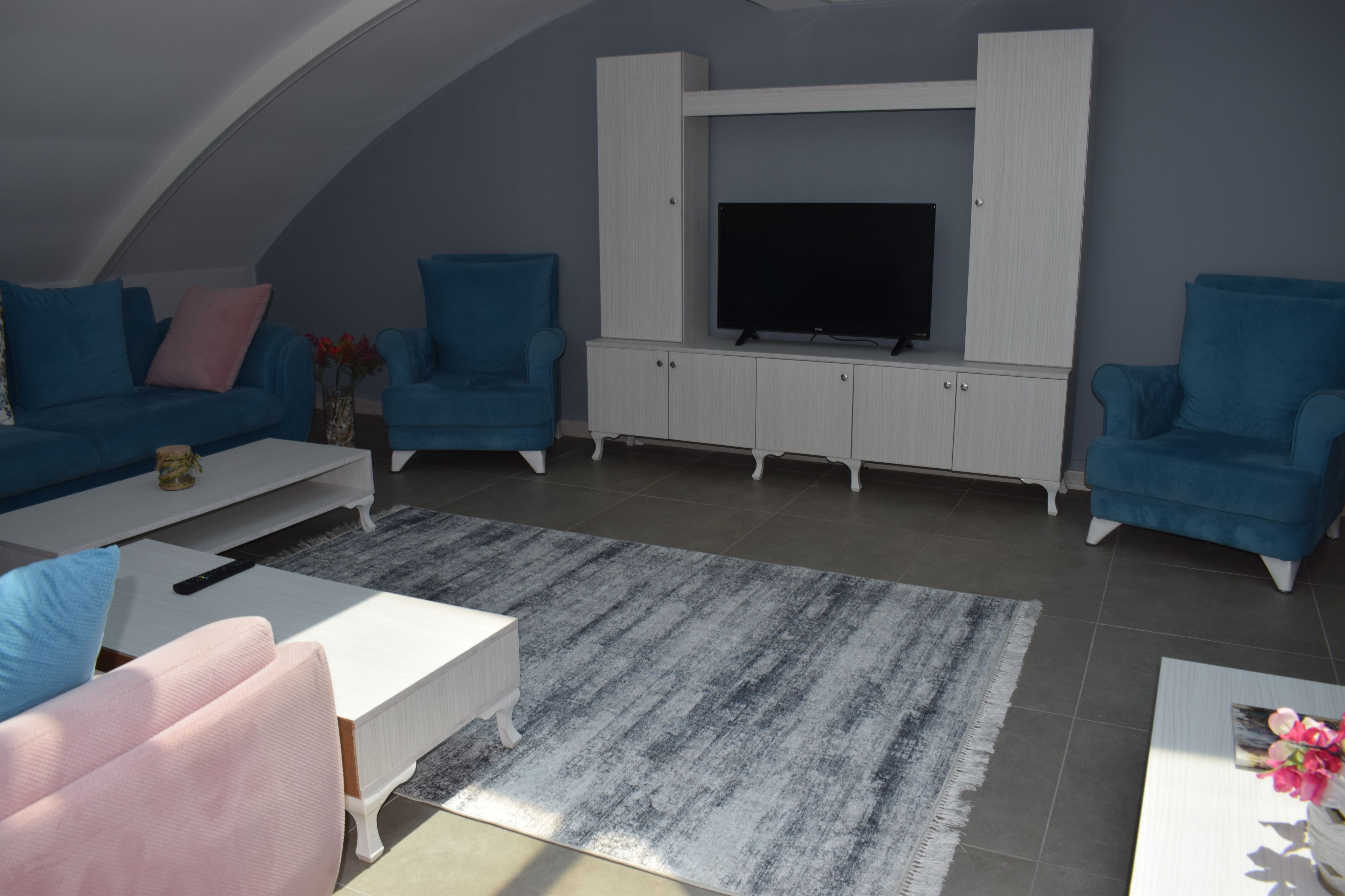 A living room with a TV, blue armchairs, a white sofa, and a coffee table.