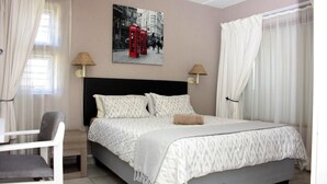 Une chambre à coucher bien rangée, avec un lit, des lampes de chevet, une chaise et un tableau représentant des cabines téléphoniques rouges accroché au mur.