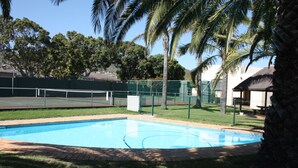 Une piscine entourée de palmiers et un court de tennis.