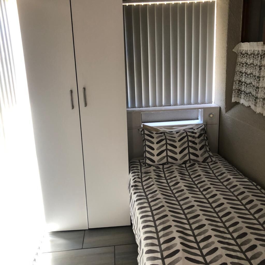 Ein Schlafzimmer mit einem Bett, einem Fenster mit Jalousien, einem Kleiderschrank und einem kleinen Tisch.