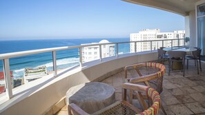 Een balkon met uitzicht op de oceaan, een ronde tafel en twee rieten stoelen.