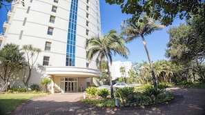 A multi-story hotel with a curved entrance, surrounded by palm trees and a landscaped garden.