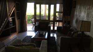 Una sala de estar con sofá, sillones, una mesa de centro y un mueble para televisión. Hay un balcón con vistas a zonas verdes.