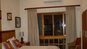 Un dormitorio con cama, ventilador de techo, ventana con cortinas, una silla y un armario.
