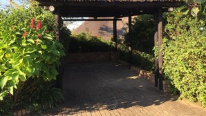 Un patio techado con piso de ladrillo, rodeado de abundante vegetación y vistas a montañas distantes.