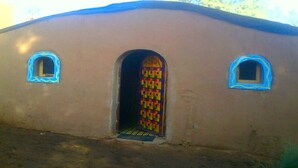 A building with a single arched doorway and two small windows with blue frames. - Locals Under Stars Trips (M'Hamid El Ghizlane)