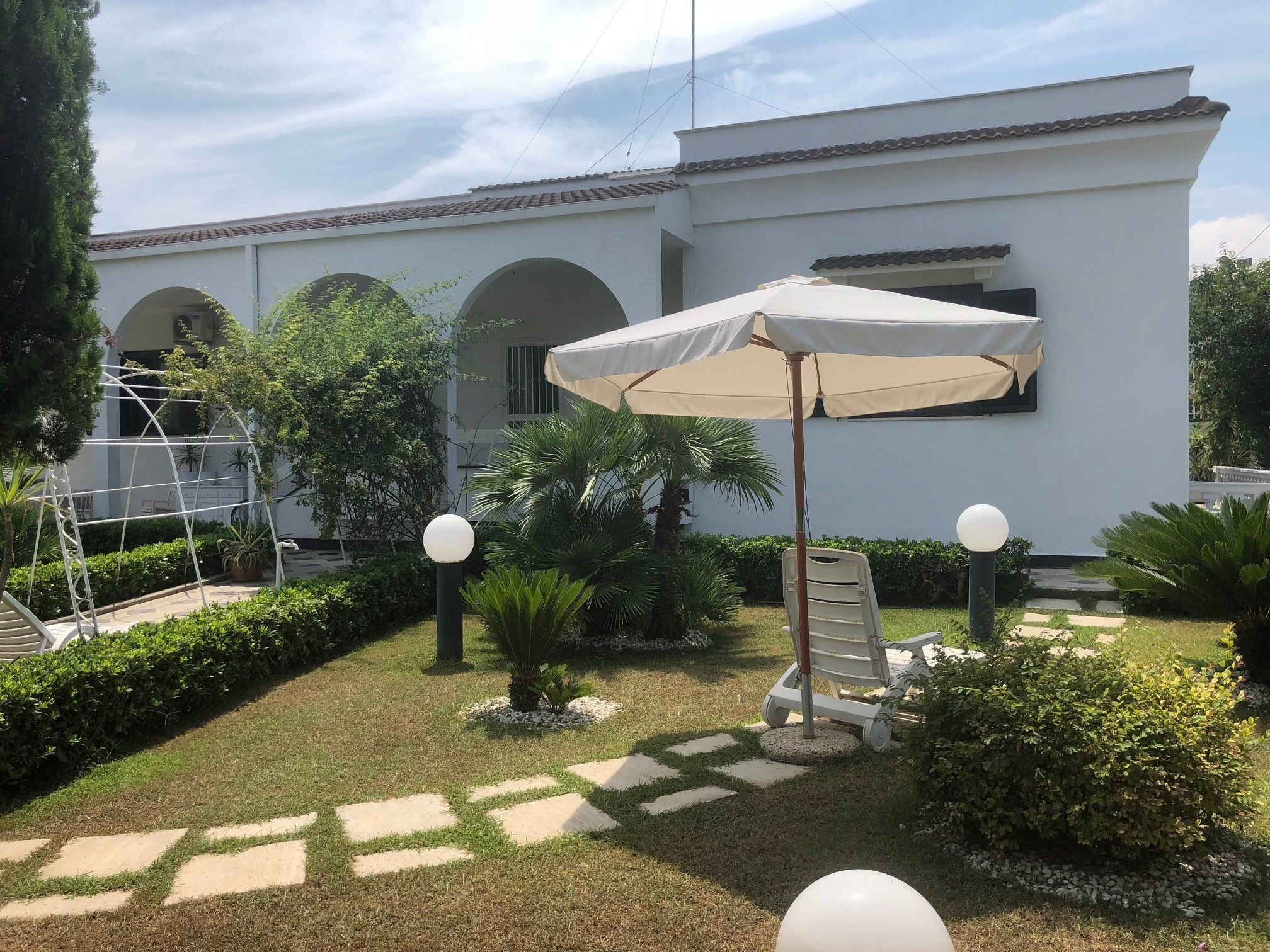 A courtyard with a white building, a covered seating area, and a pergola structure.