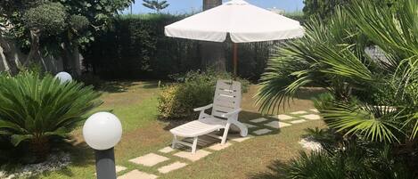 A garden with a white umbrella, a white chair, and a variety of plants.