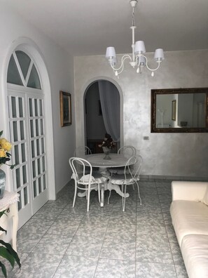 A dining area with a round table and chairs, a chandelier, a mirror, and a white sofa. - Villa Nicolaus (Bari)